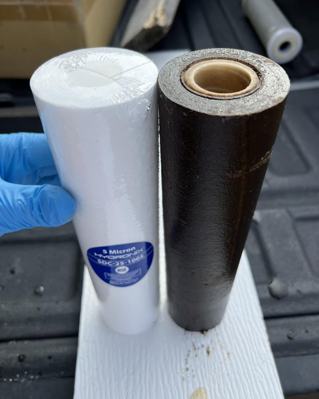A new white filter held next to a filthy used filter from a customer's system
